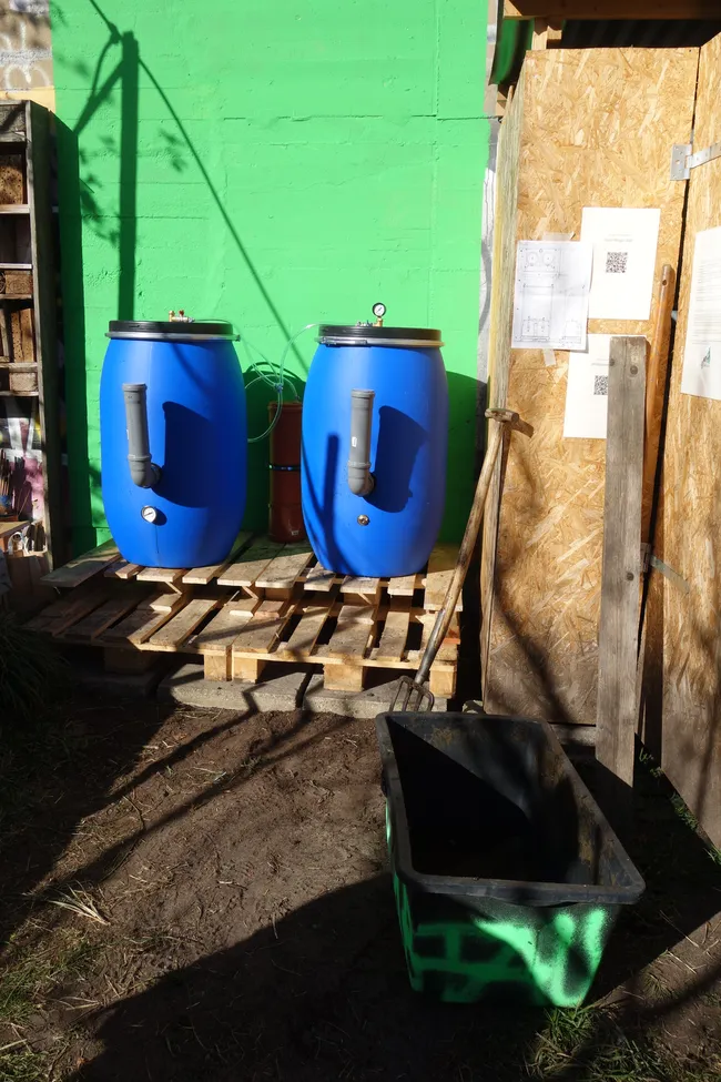 Die fertige Anlage: blaue Fässer vor grüner Wand.
